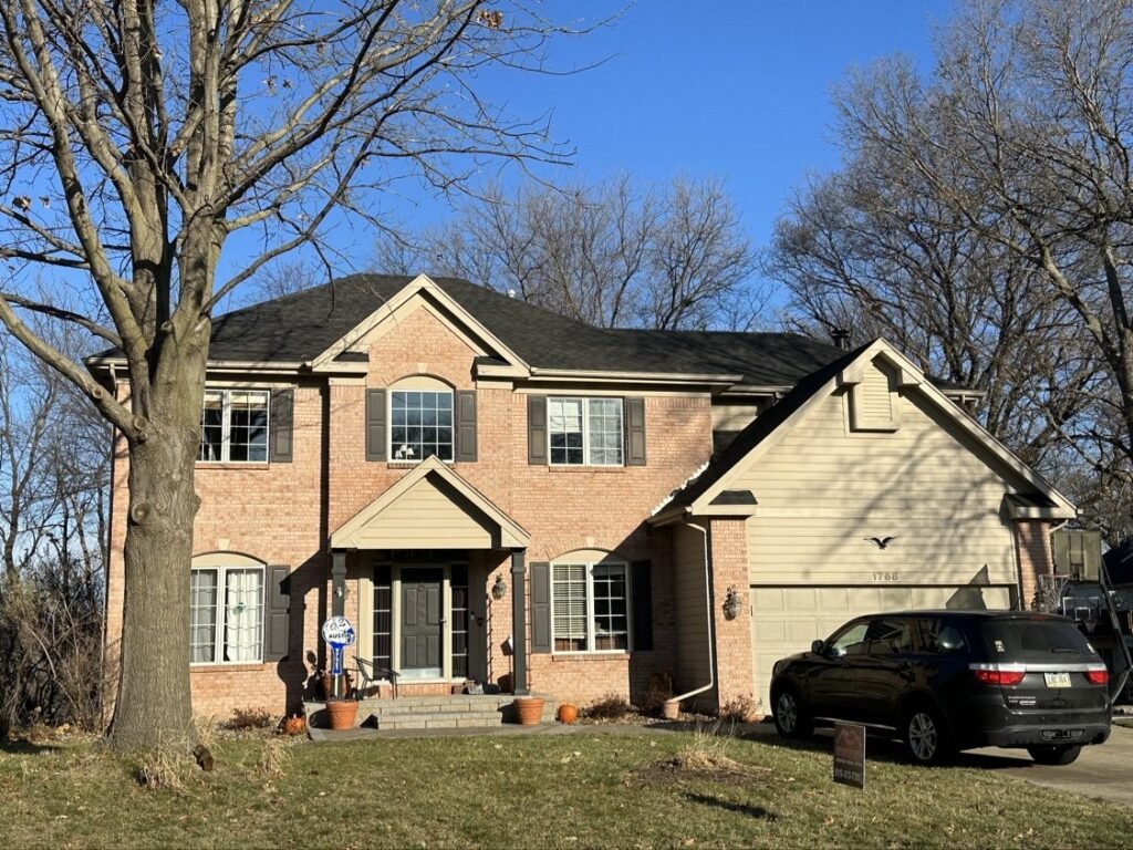 Completed dark shingle roof on a brick two-story home by Hutch Unlimited Roofing, Iowa