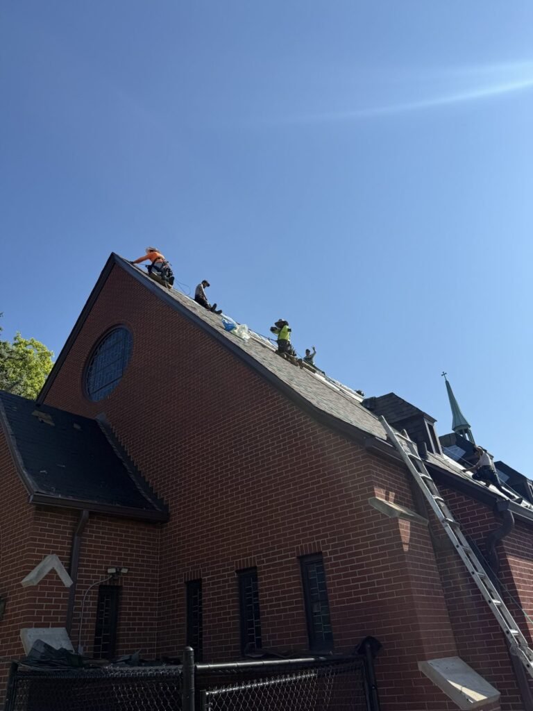 Roofers working on a steep church roof ridge by Hutch Unlimited Roofing, Iowa