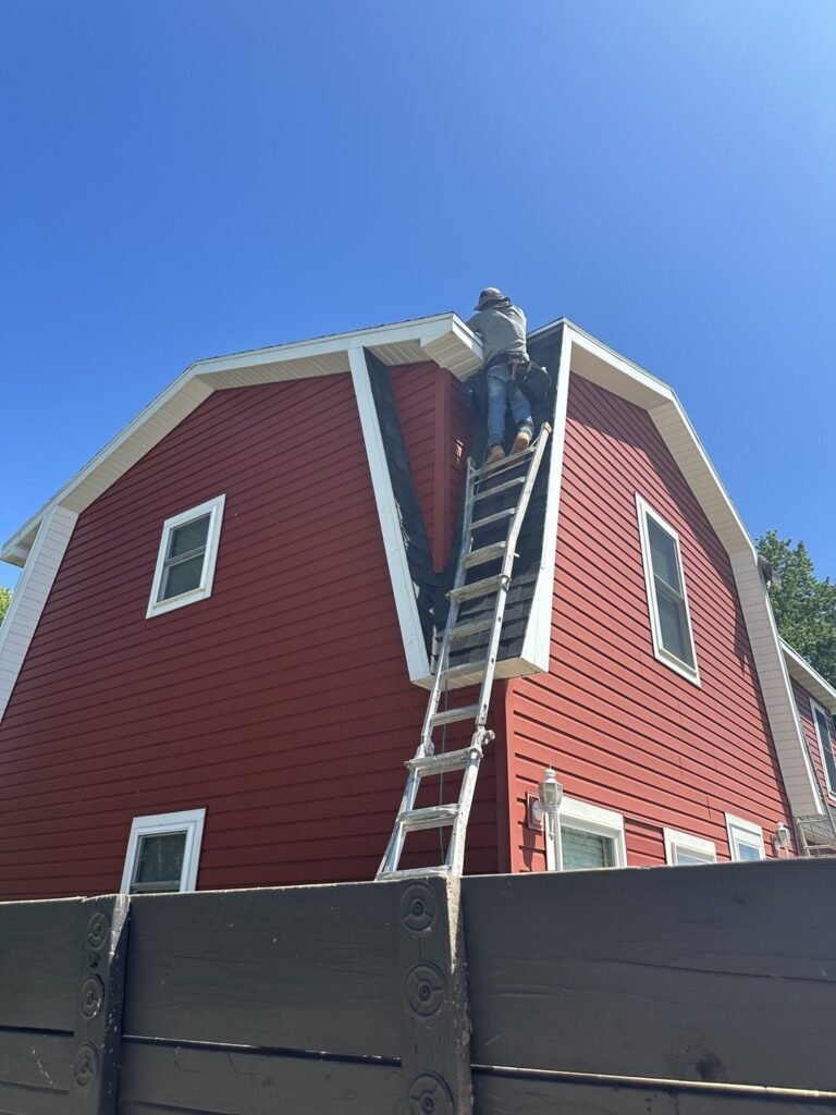 Hutch Unlimited Roofing worker installing shingles on a gambrel roof gable, Iowa